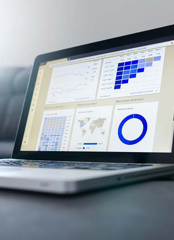 Open laptop displaying various digital analytics charts including bar graphs, maps, and pie charts on screen.