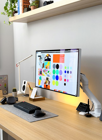 Modern workspace with a wooden desk featuring a monitor displaying colorful graphics, keyboard, mouse, and desk lamp.