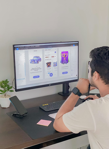 Man with smartwatch working at a desk looking at a large monitor displaying app interface designs.